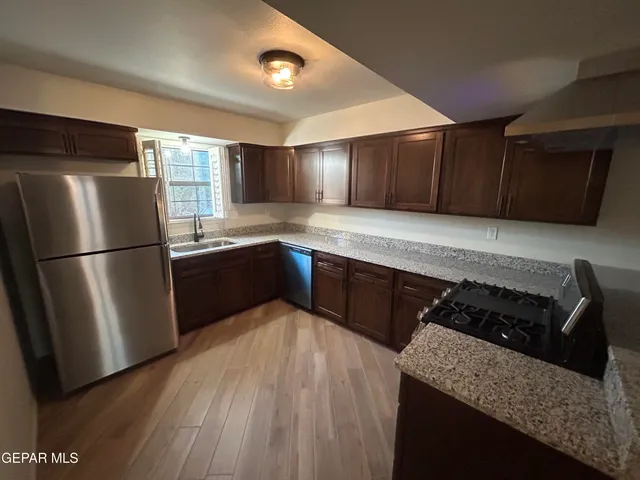 a kitchen with granite countertop stainless steel appliances a refrigerator a sink and wooden cabinets