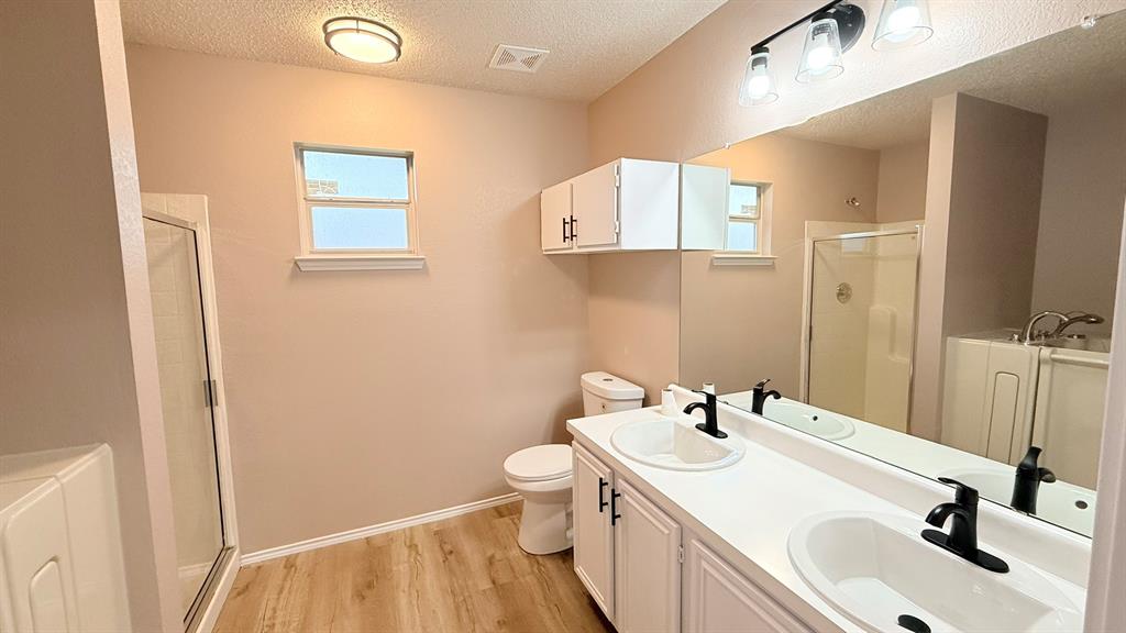12259 Rim Rock Road Dallas, TX 75253 - Photo 9 of 17 Bathroom featuring a textured ceiling, a shower stall, double vanity, light wood finished floors, and a garden tub