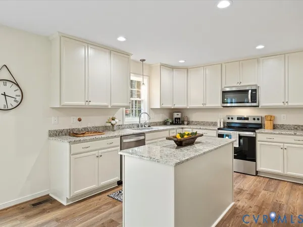 a kitchen with stainless steel appliances granite countertop a stove top oven a sink a refrigerator and white cabinets with wooden floor