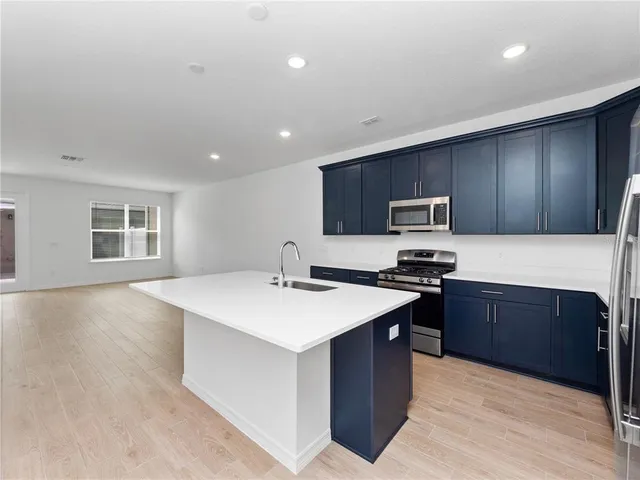 a large kitchen with stainless steel appliances a sink dishwasher stove top oven and wooden cabinets