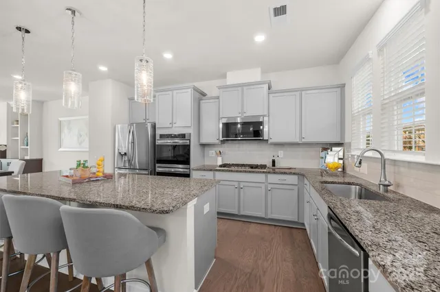 a kitchen with stainless steel appliances granite countertop a stove top oven a sink dishwasher a dining table and chairs with wooden floor