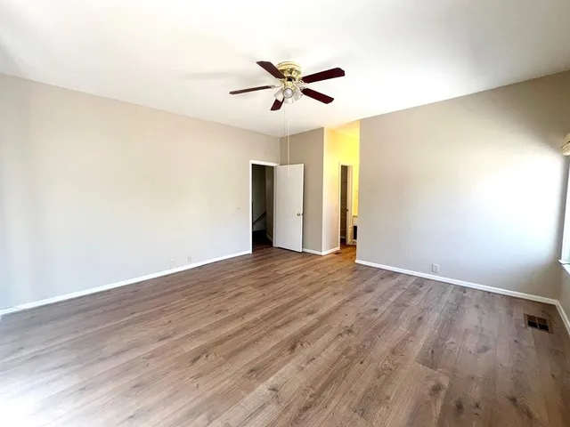 an empty room with wooden floor ceiling fan and windows