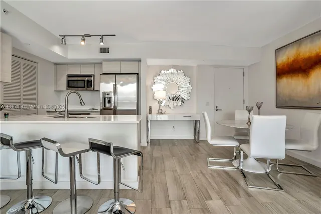 a dining hall with stainless steel appliances kitchen island granite countertop a dining table chairs and a refrigerator