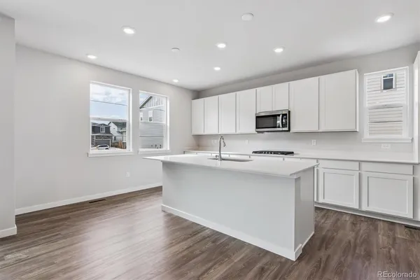 a open kitchen with kitchen island a sink dishwasher a stove and white cabinets with wooden floor