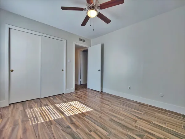 a view of an empty room with wooden floor and a ceiling fan