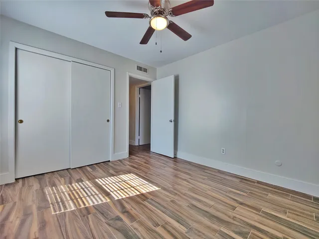 a view of an empty room with wooden floor and a ceiling fan