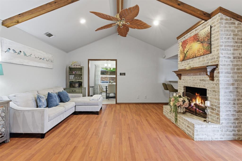 2307 Castle Rock Road Carrollton, TX 75007 - Photo 9 of 34 Spacious living room featuring a vaulted ceiling with exposed wooden beams, hardwood flooring, and a brick fireplace with a wooden mantel