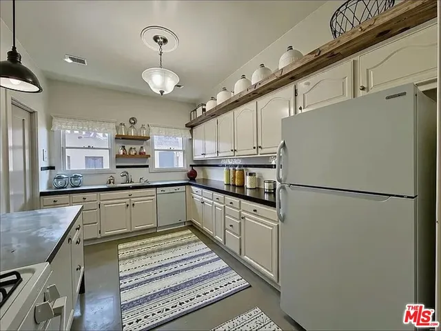 a kitchen with granite countertop a refrigerator a stove and white cabinets with wooden floor