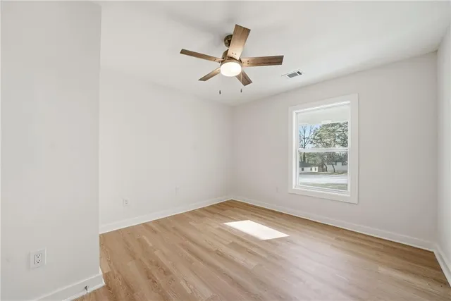 an empty room with wooden floor ceiling fan and windows