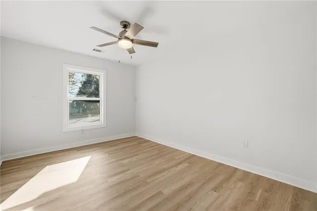 an empty room with wooden floor chandelier fan and windows