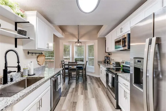 a kitchen with stainless steel appliances granite countertop a refrigerator a stove top oven a sink dishwasher and white cabinets with wooden floor