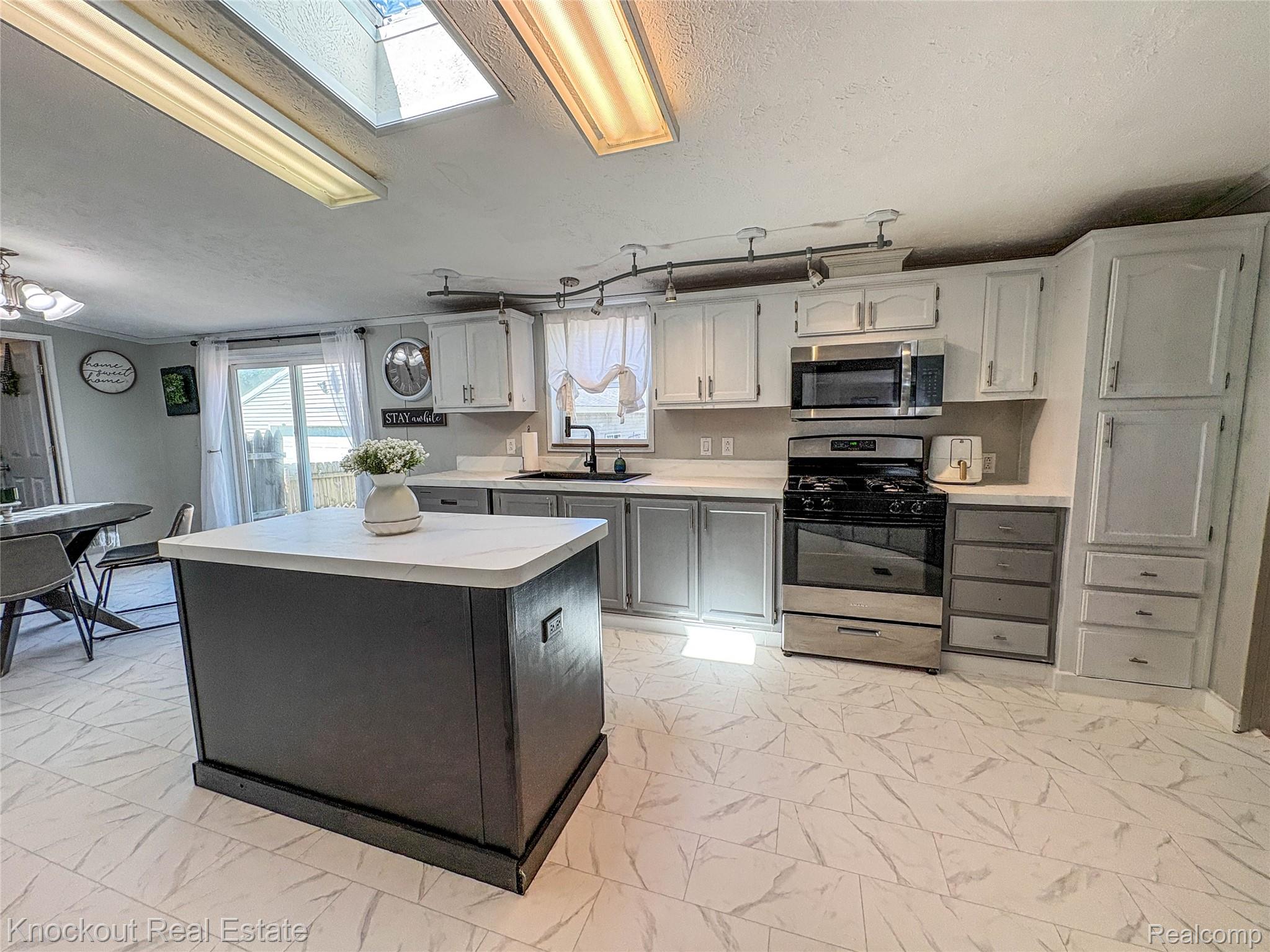 7760 Bell Road Birch Run, MI 48415 - Photo 15 of 68 Kitchen featuring a central island with a light-toned countertop, stainless steel appliances, a combination of white and gray cabinetry, and patterned tile flooring