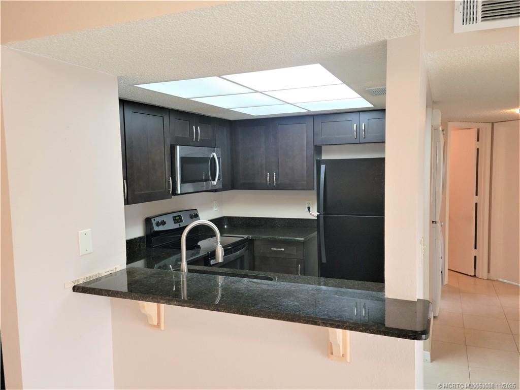 1526 Southeast Royal Green Circle, Unit 205 Port St. Lucie, FL 34952 - Photo 15 of 34 a kitchen with kitchen island granite countertop a sink and a refrigerator