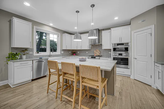 a kitchen with a dining table chairs wooden floor cabinets and appliances