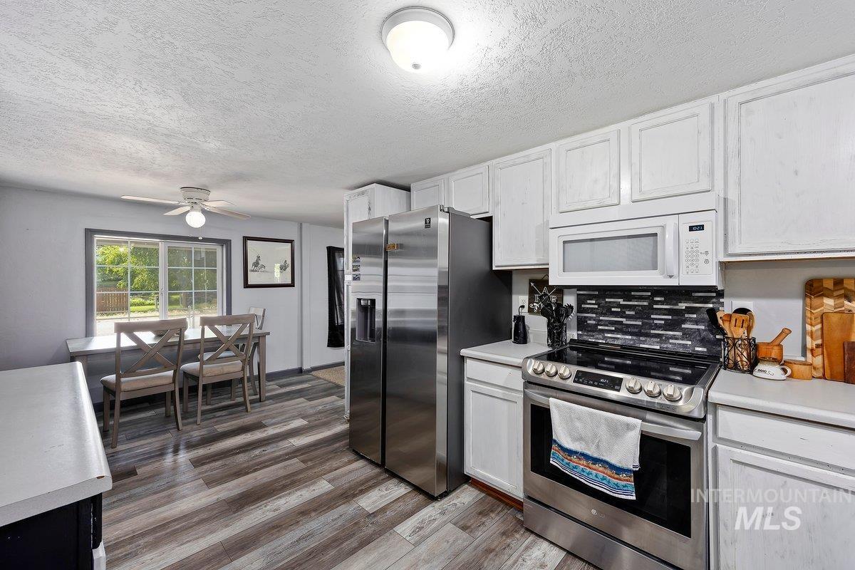418 South Date Street Shoshone, ID 83352 - Photo 10 of 36 Kitchen featuring stainless steel appliances, white cabinetry, a mosaic tile backsplash, and wood-finish flooring