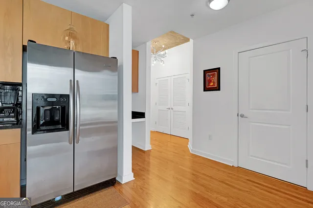 a view of a refrigerator in kitchen and an empty room with wooden floor