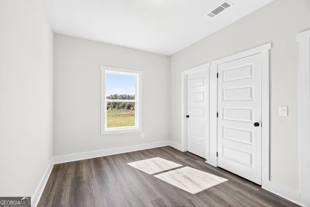 an empty room with wooden floor closet and windows