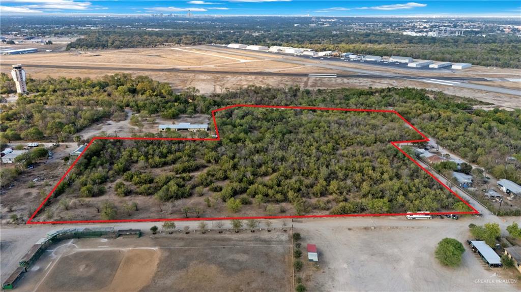 Expansive land parcel featuring a perimeter marked in red, substantial tree coverage, and existing structures within the boundaries