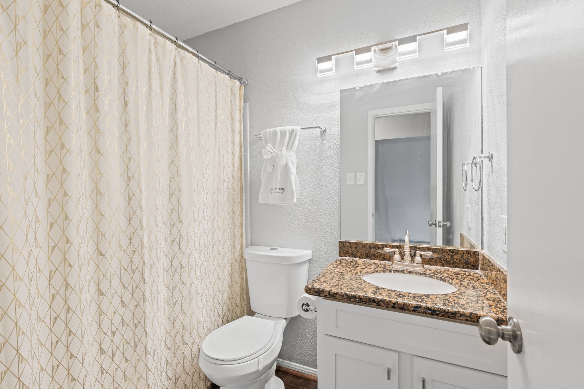 2211 South Kirkwood Road, Unit 1 Houston, TX 77077 - Photo 12 of 16 The secondary bath carries the same dark speckled granite countertop as the kitchen and primary bath — a consistent finish language that runs through every wet space in the unit. A tub/shower combination occupies the left wall, and a modern rectangular light bar above the mirror keeps the space well lit.
