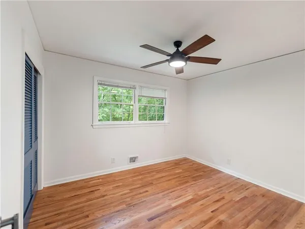 an empty room with wooden floor ceiling fan and windows