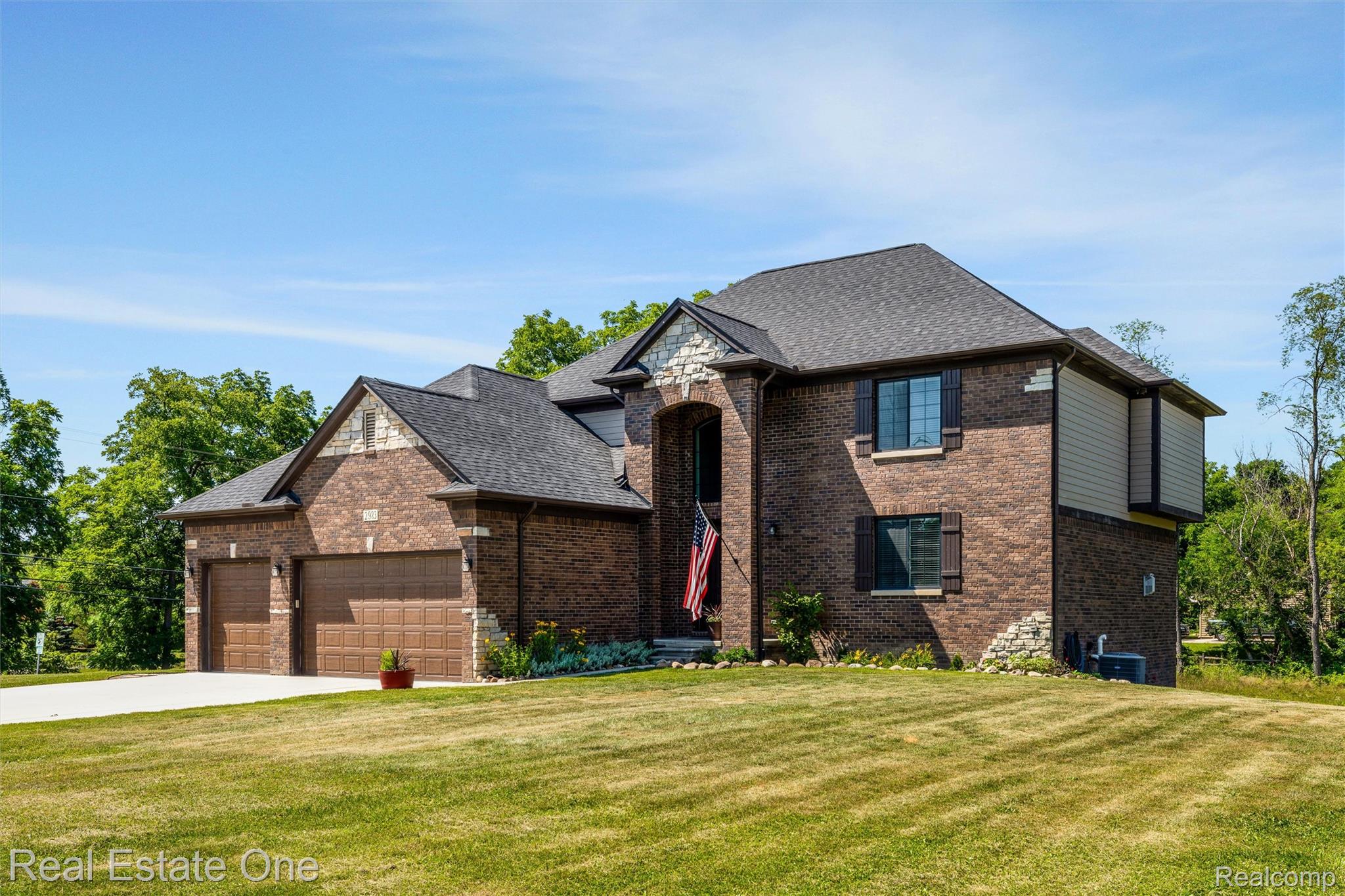 2983 28 Mile Road Washington, MI 48094 - Photo 36 of 54 Brick and stone facade residence featuring a multi-car garage, dark-shingle roof, decorative window shutters, a prominent arched entry, and a well-maintained lawn