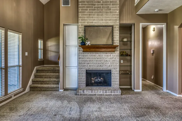 a view of an empty room with wooden floor fire place and windows