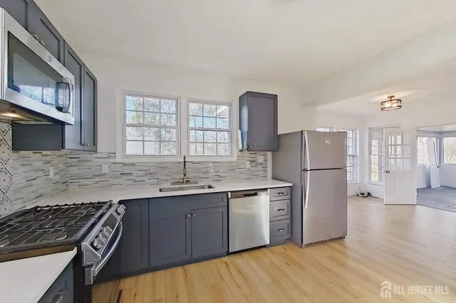 a kitchen with stainless steel appliances granite countertop a stove a sink dishwasher a refrigerator and white cabinets with wooden floor