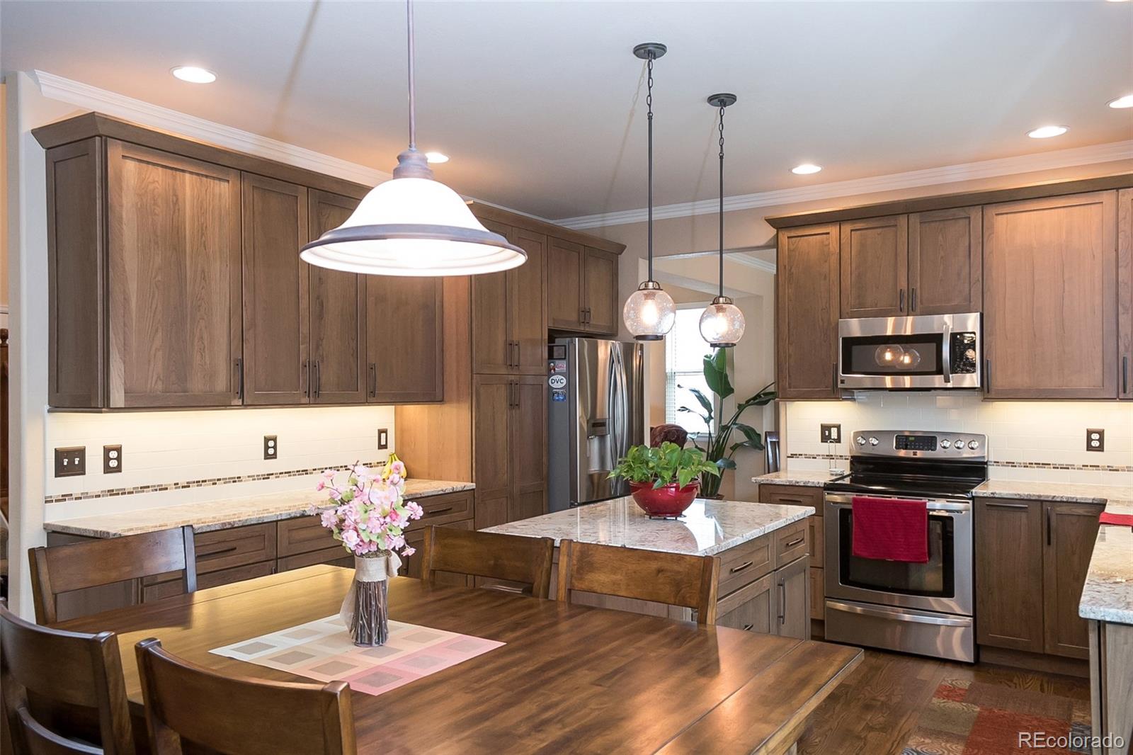 10221 South Nickolas Avenue Highlands Ranch, CO 80130 - Photo 11 of 35 a living room with stainless steel appliances kitchen island granite countertop a stove a refrigerator a kitchen island a dining table and chairs with wooden floor
