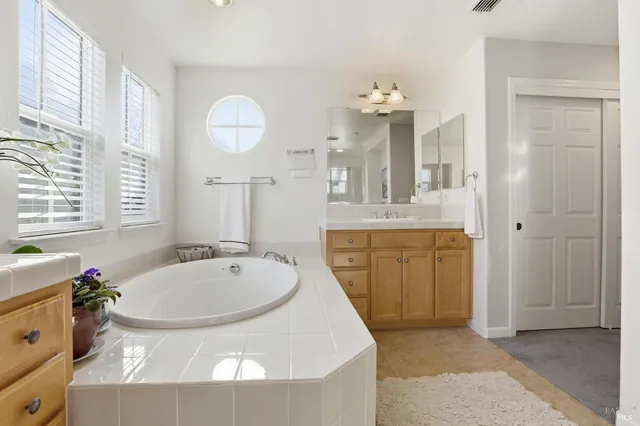 a spacious bathroom with a granite countertop sink a mirror a bathtub and a window