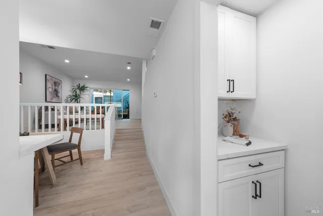 a hallway with wooden floor a dining table chairs and a white refrigerator