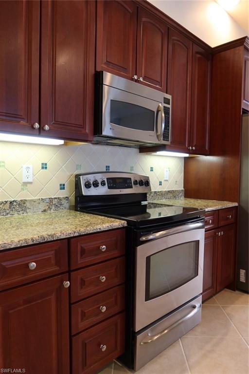 7168 Lemuria Circle, Unit 1701 Naples, FL 34109 - Photo 10 of 39 Stainless steel range and microwave oven complementing rich wood-finish cabinetry, granite countertops, and a tile backsplash with decorative accents