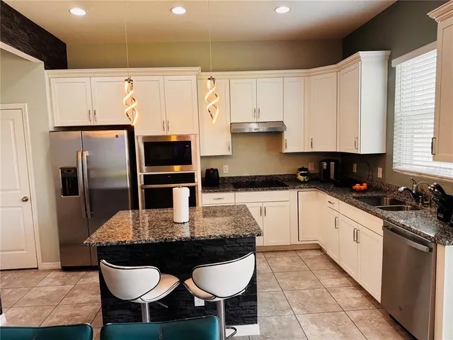 a kitchen with stainless steel appliances granite countertop a sink a stove a refrigerator and white cabinets