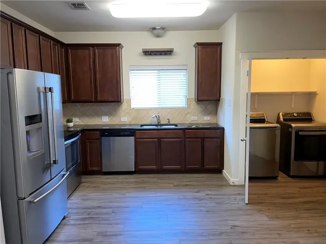 a kitchen with granite countertop wooden floors stainless steel appliances a sink and a window