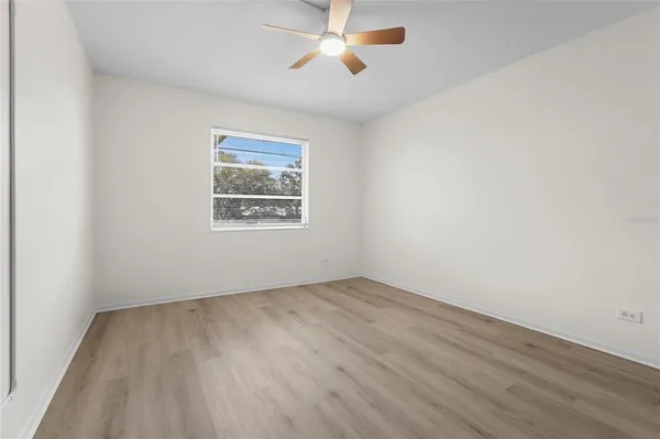 an empty room with wooden floor ceiling fan and windows