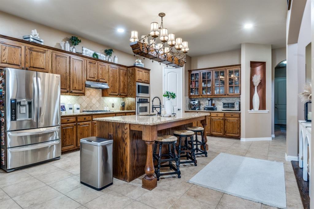 2810 Baker Street Sachse, TX 75048 - Photo 7 of 26 Kitchen featuring appliances with stainless steel finishes, arched walkways, brown cabinetry, a kitchen bar, and recessed lighting