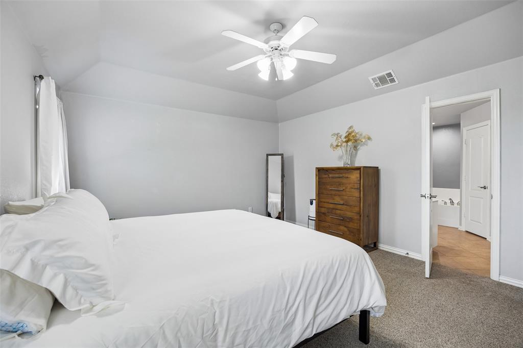 11211 Emerald Ranch Lane Forney, TX 75126 - Photo 23 of 35 Primary Carpeted interior space featuring a ceiling fan with light fixture, vaulted ceiling, and an open doorway revealing a partial bathtub