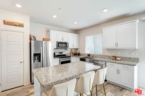 a kitchen with stainless steel appliances granite countertop a stove top oven a refrigerator a sink and dishwasher with wooden floor