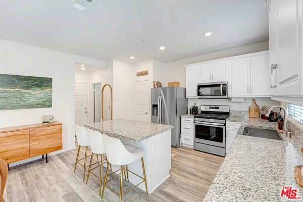 a kitchen with stainless steel appliances granite countertop a stove top oven a sink dishwasher and a refrigerator with wooden floor