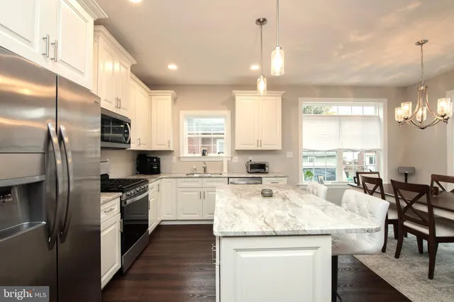 a kitchen with kitchen island granite countertop a stove a sink a oven a refrigerator and white cabinets with wooden floor