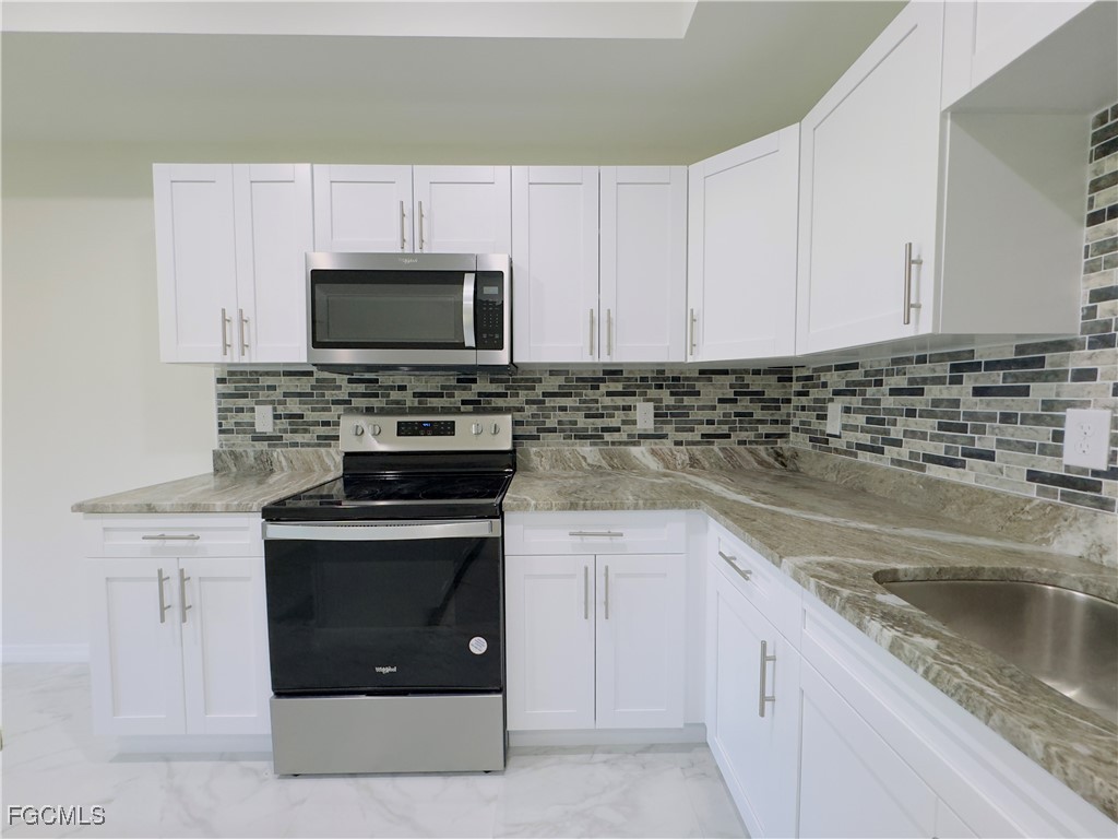884 Alabama Road South Lehigh Acres, FL 33974 - Photo 13 of 37 a kitchen with granite countertop a stove sink and microwave