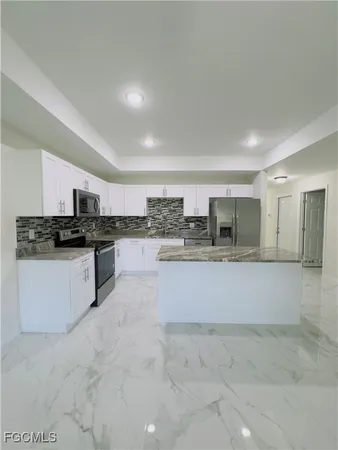 a large white kitchen with stainless steel appliances granite countertop a stove and a sink