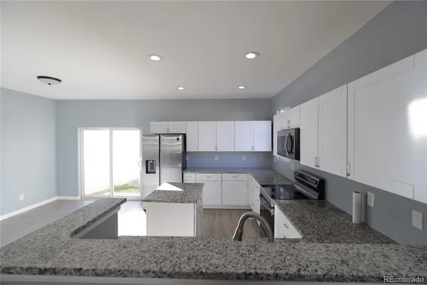 a kitchen with kitchen island granite countertop a sink a stove a counter space and cabinets