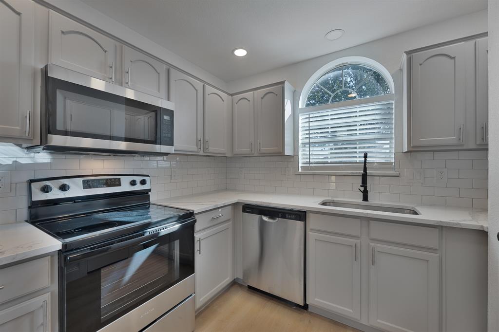 Kitchen with stainless steel appliances, light stone countertops, decorative backsplash, recessed lighting, and light wood-style flooring