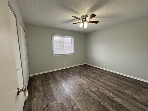 an empty room with wooden floor chandelier fan and windows