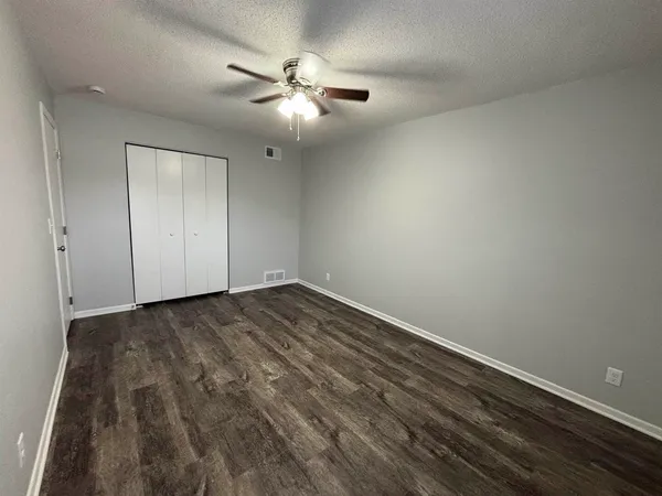 an empty room with a chandelier fan and wooden floor