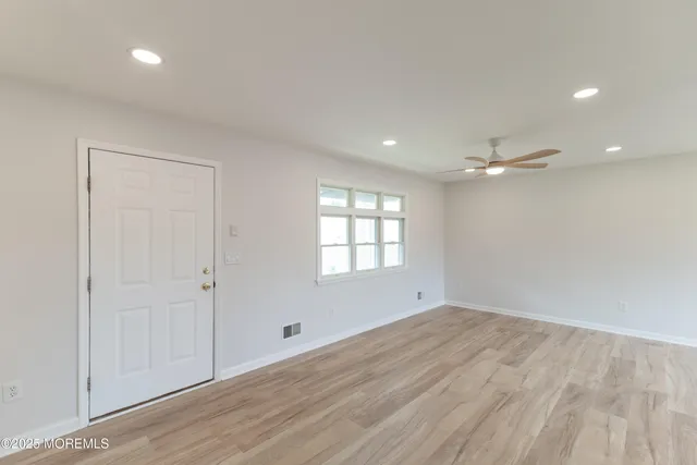 a view of an empty room and kitchen with wooden floor