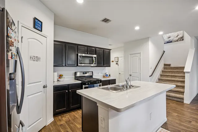 a kitchen with stainless steel appliances a sink a stove a refrigerator cabinets and a dining table