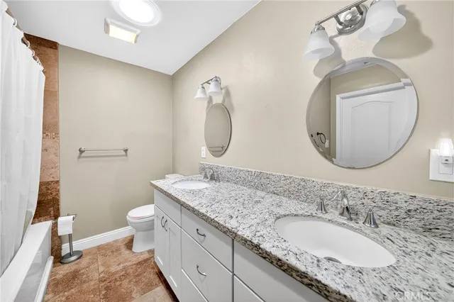 a bathroom with a granite countertop double vanity sink mirror and toilet