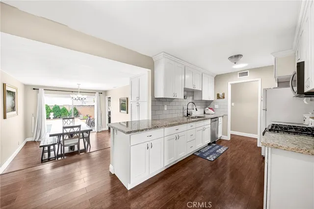 a large white kitchen with granite countertop a stove top oven a sink a dining table and chairs with wooden floor