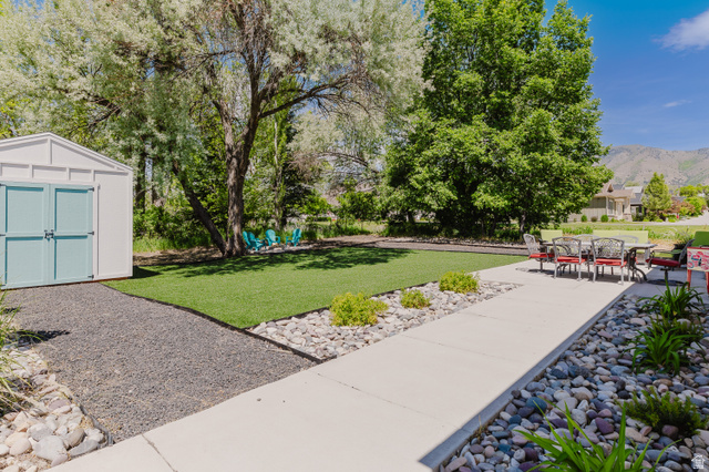 287 East 1000 North Logan, UT 84321 - Photo 40 of 41 Expansive backyard featuring a defined concrete patio, artificial turf, a gravel pathway, and a white storage shed with blue doors